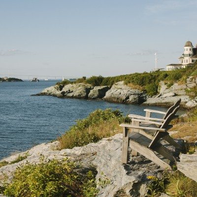 Two Adirondak chairs overlook the water in Newport, Rhode Island on a peaceful evening.